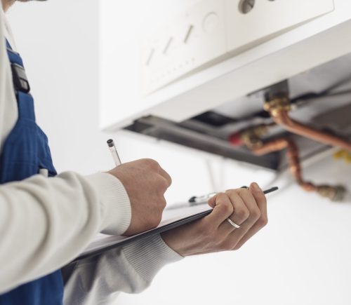Professional plumber checking a boiler at home and writing on a clipboard